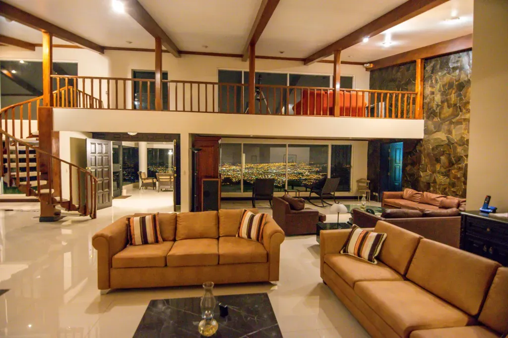 Two-story living room with leather sofas, a stone wall and glass walls overlooking the city lights